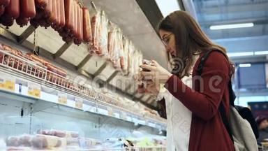 年轻女子在超市的杂货店选择香肠。